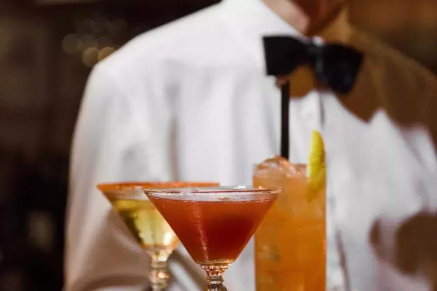 在贝博体彩app的苦艾酒餐厅，一名戴着领结的服务员端着一盘鸡尾酒.